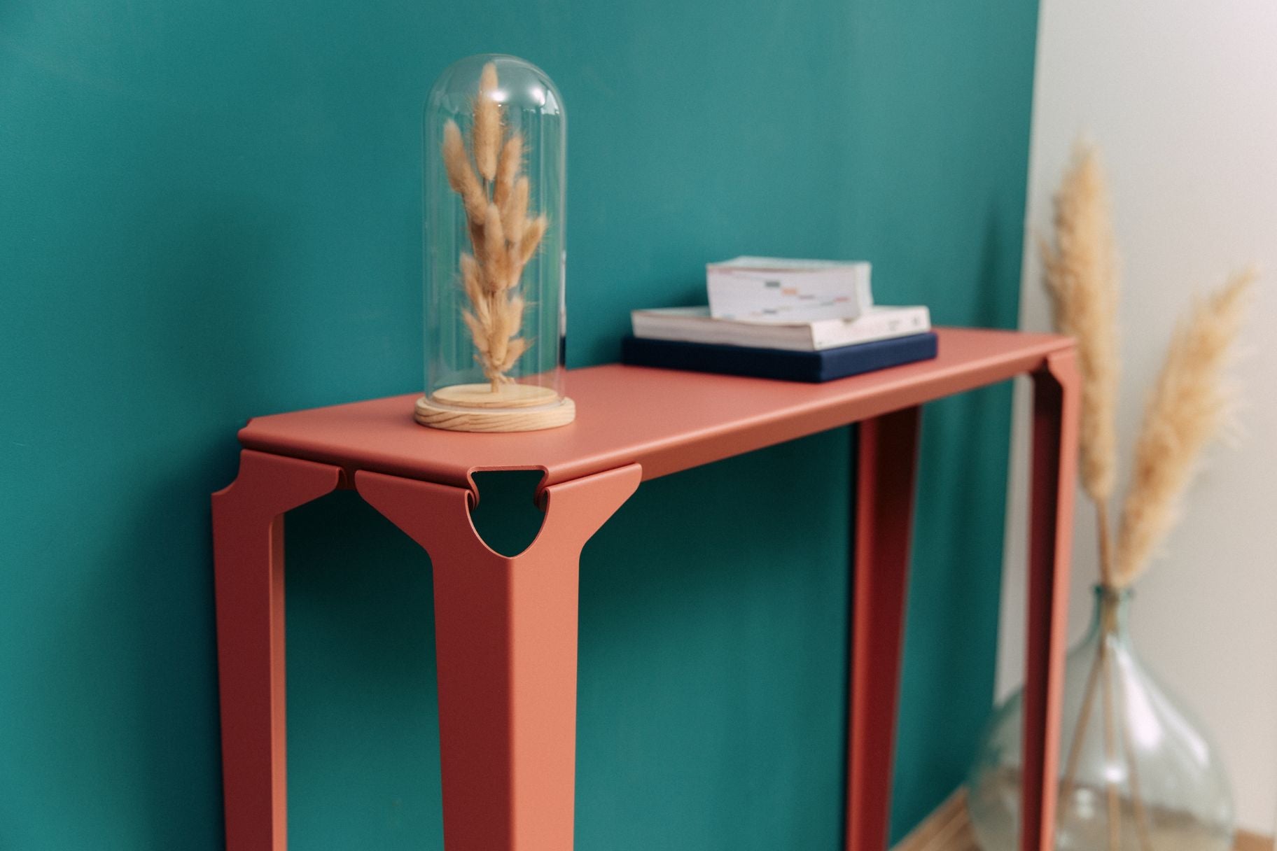 Console chantilly en acier rose avec des livres et une fleur séché sous cloche en verre