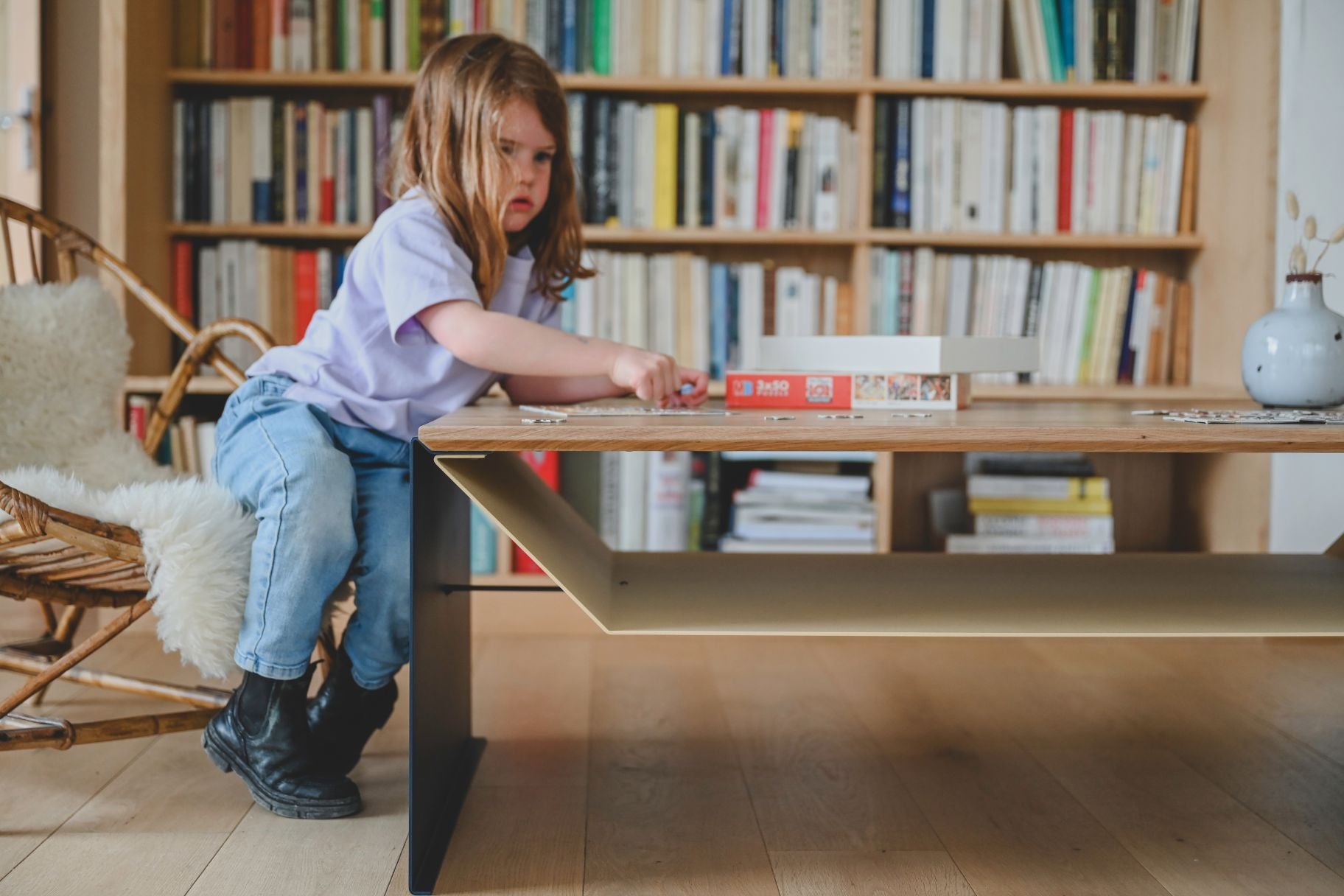 Table de salon design en chêne massif et acier avec rangement devant une cheminée et une bibliothèque