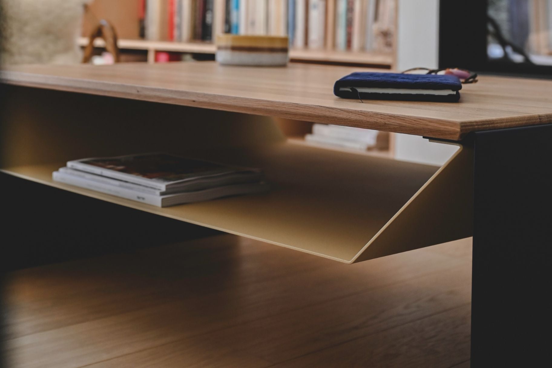 Table de salon design en chêne massif et acier avec rangement devant une cheminée et une bibliothèque