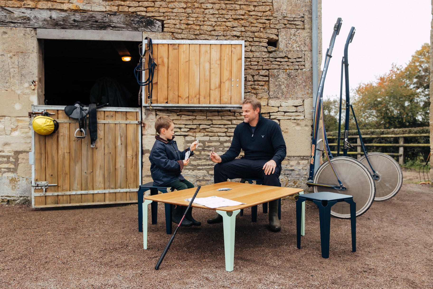 famille jouant aux cartes sur une table basse bois et acier Biarritz de couleur vert pastel au milieu d'un haras