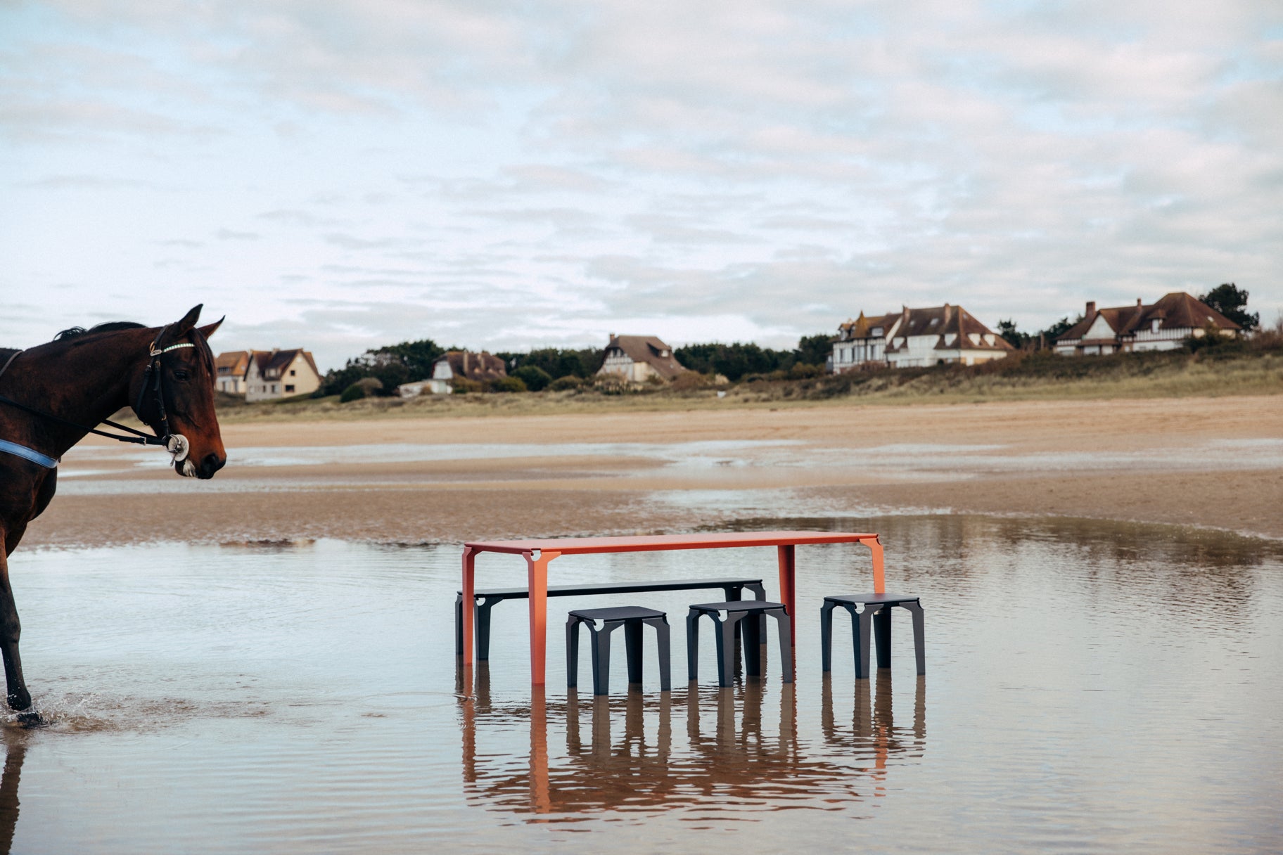 Tabourets et banc acier de couleur bleu acier autour d'une table rose au milieu de l'eau à la plage