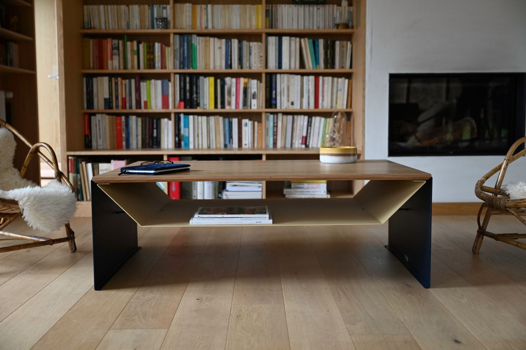 Table de salon design en chêne massif et acier avec rangement devant une cheminée et une bibliothèque