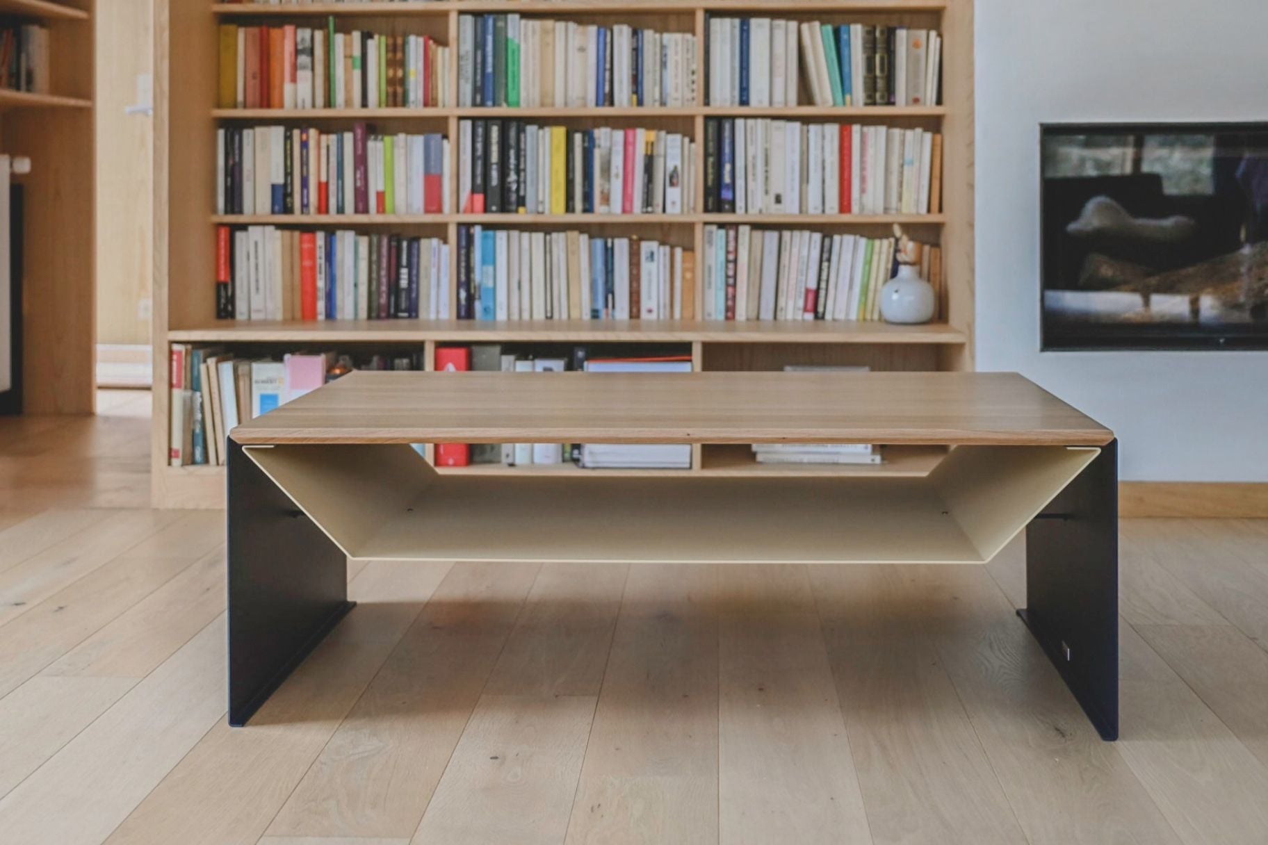 Table de salon design en chêne massif et acier avec rangement devant une cheminée et une bibliothèque