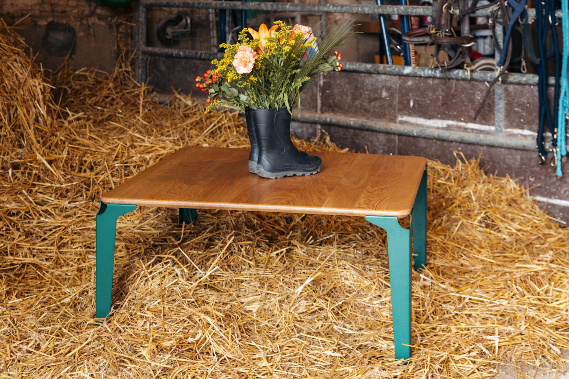 table basse bois et acier Biarritz de couleur vert mousse posée dans la paille avec un bouquet de fleurs