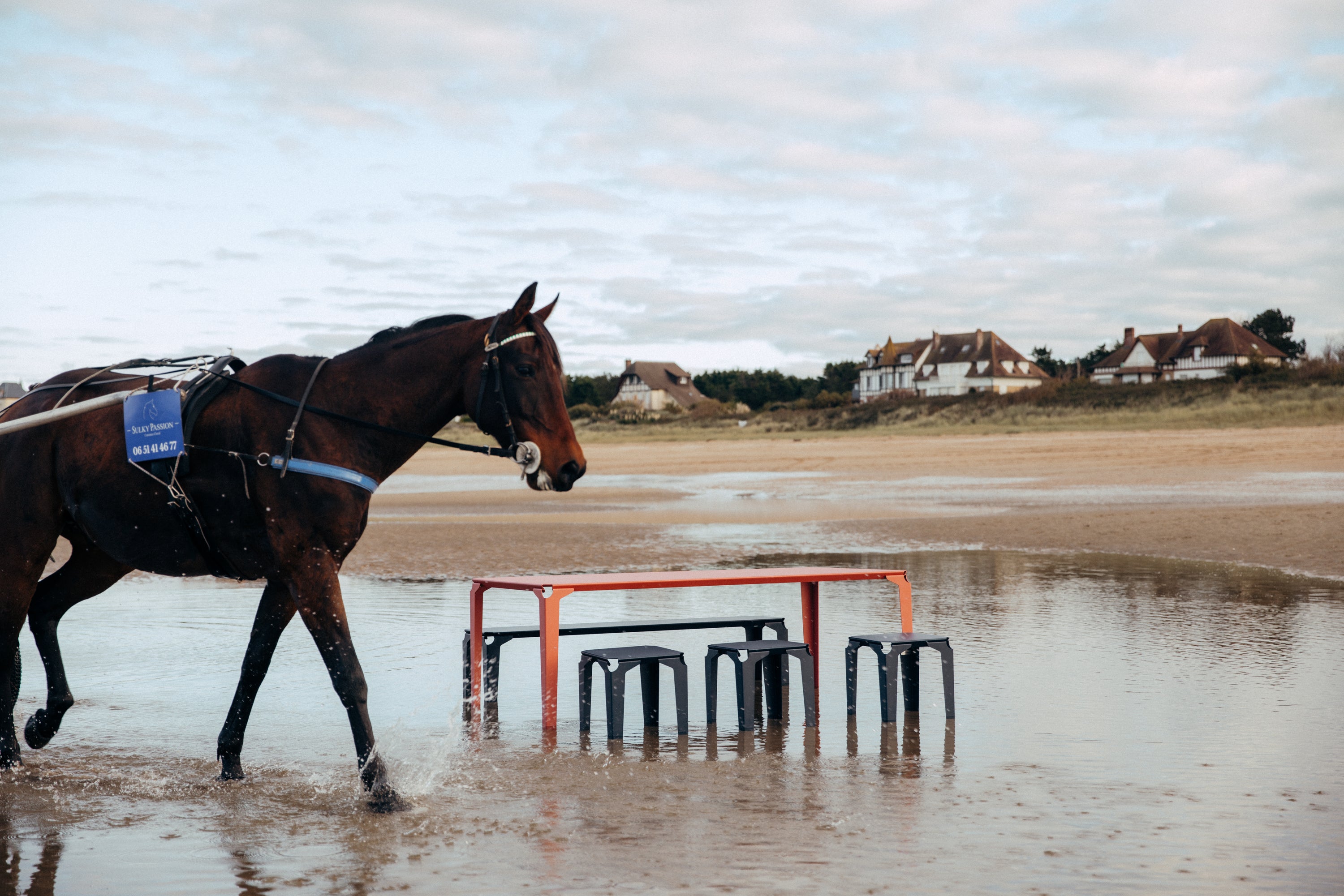 cheval les pieds dans l'eautournant autour d'une table et de tabouret en acier atelier percheron à la plage de cabourg